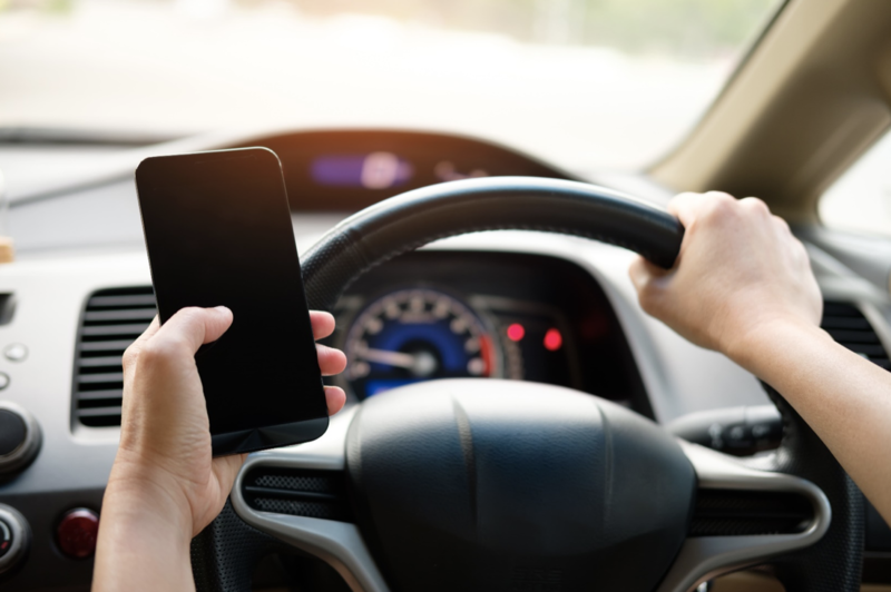 Hands holding black smartphone and car steering wheel