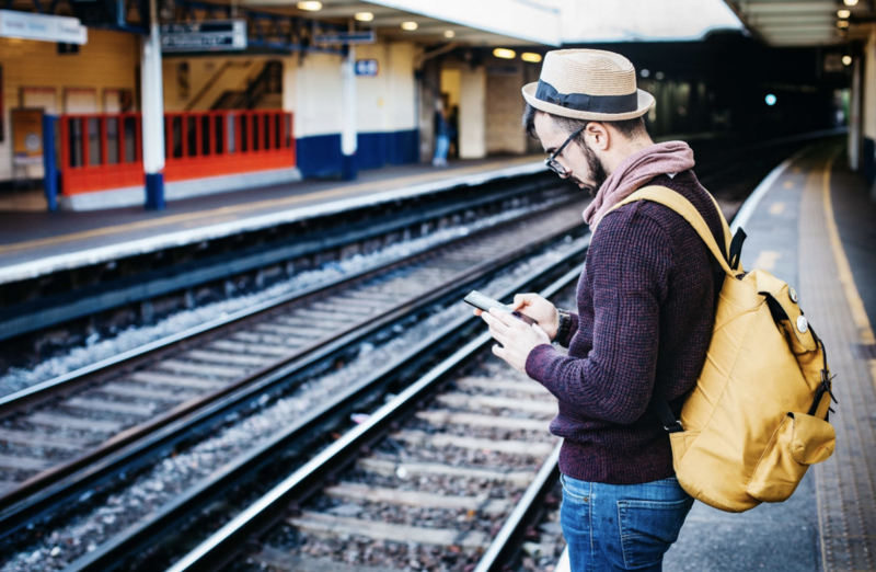 Male tourist using travel app on train station platform