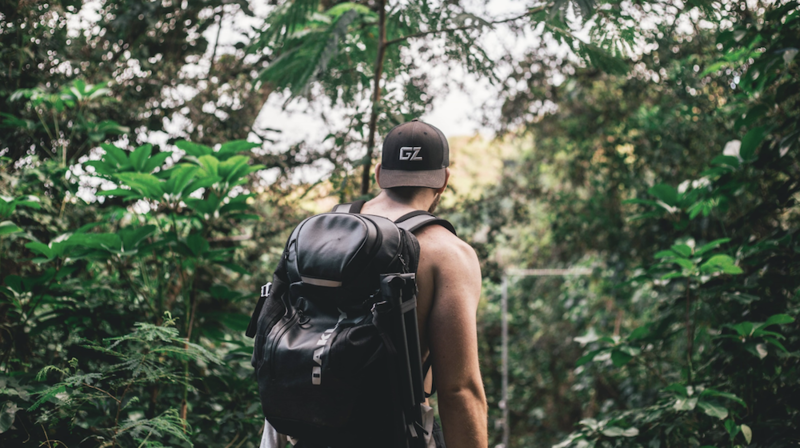 A man with a backpack hiking in the woods from behind