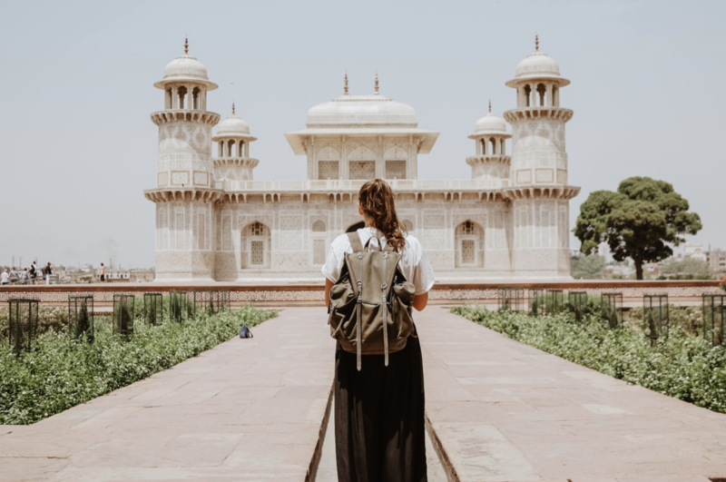 Girl with backpack facing away from camera standing before white historical building in Agra, India
